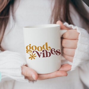 May include: White ceramic mug with the text "good vibes" in yellow and maroon lettering with a small flower graphic.