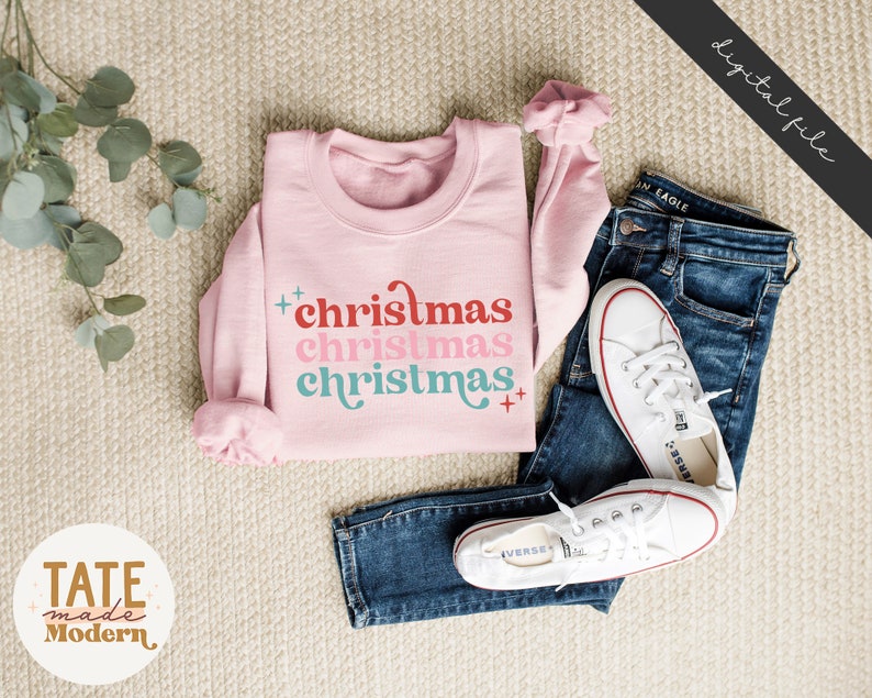 Pode incluir: Camisola cor-de-rosa com o texto "christmas christmas christmas" numa fonte retro com cores vermelho, rosa e azul.