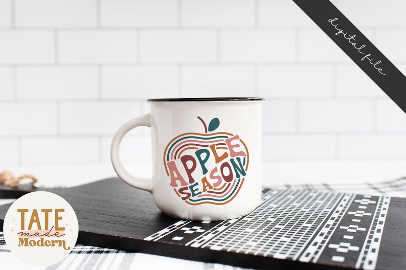 May include: White ceramic mug with a black rim and handle. The mug features a graphic of an apple with the text "Apple Season" inside the apple. The text is in a colorful, retro font.