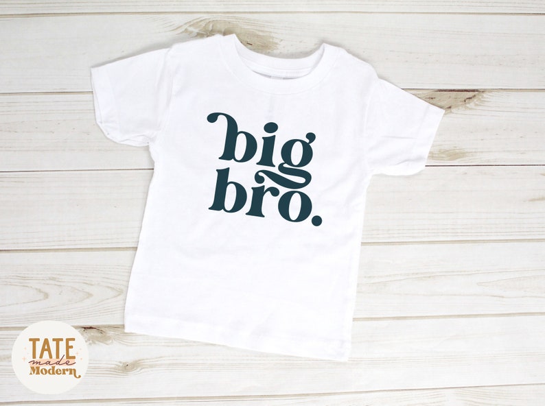Puede incluir: Camiseta blanca con el texto "big bro." en fuente azul oscuro.