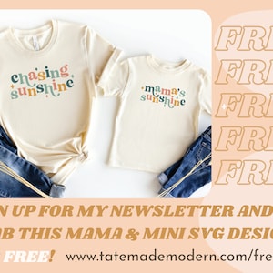 May include: Two cream-colored t-shirts with the text "chasing sunshine" and "mama's sunshine" in colorful letters. The shirts are folded and displayed on a white background with blue jeans and dried grass.