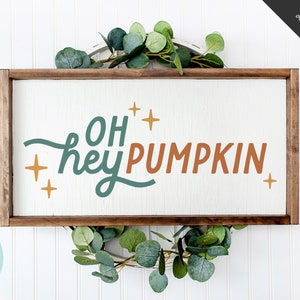 May include: A wooden sign with the text "Oh hey pumpkin" in teal and orange lettering with gold stars. The sign is framed in a brown wood frame and is sitting on a white background.
