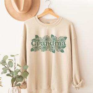 May include: A beige sweatshirt with a green graphic of the word "Grandma" surrounded by stylized sunflowers.