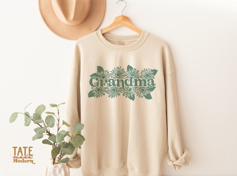 May include: A beige sweatshirt with a green graphic of the word "Grandma" surrounded by stylized sunflowers.
