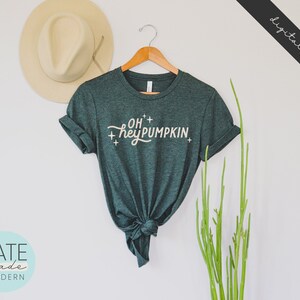 May include: A dark green t-shirt with the text "OH+ hey PUMPKIN+ " in a white script font.