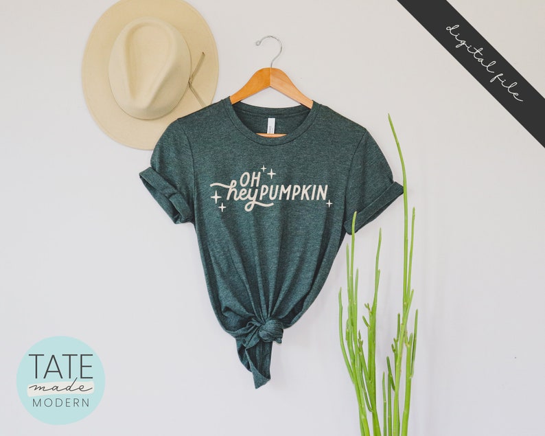 May include: A dark green t-shirt with the text "OH+ hey PUMPKIN+ " in a white script font.