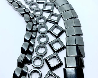 May include: A collection of black hematite beads in various shapes, including round, oval, square, and rectangular. The beads are strung on a clear thread and are ready for jewelry making.