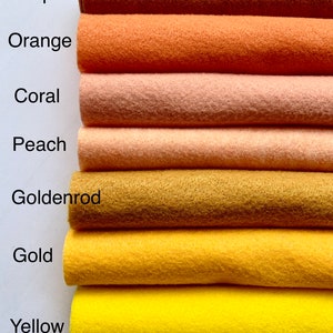 May include: A stack of seven felt fabric swatches in shades of orange, yellow, and brown. The swatches are labeled from top to bottom: Pumpkin, Orange, Coral, Peach, Goldenrod, Gold, and Yellow.