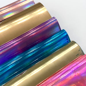 Op de afbeelding: Een set van zes iriserende vinylvellen in verschillende kleuren, waaronder goud, paars, blauw en roze. De vellen zijn in een waaier vorm gerangschikt, met het gouden vel bovenaan en het roze vel onderaan.