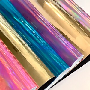 Op de afbeelding: Vijf rollen iriserende vinyl in verschillende kleuren, waaronder goud, teal, paars en roze. De vinyl is glanzend en reflecterend.