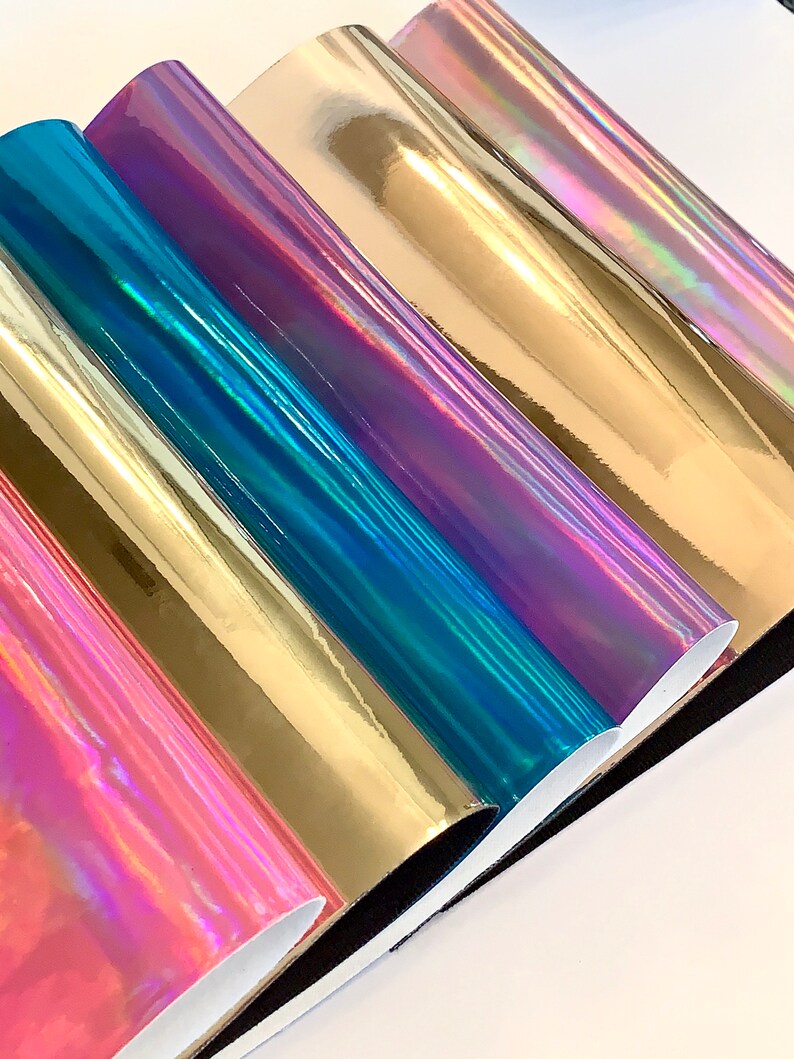 Op de afbeelding: Vijf rollen iriserende vinyl in verschillende kleuren, waaronder goud, teal, paars en roze. De vinyl is glanzend en reflecterend.