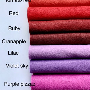 May include: A stack of seven felt fabric strips in various shades of red, purple, and pink. The strips are labeled with the names "Tomato red", "Red", "Ruby", "Cranapple", "Lilac", "Violet sky", and "Purple pizzaz".