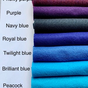 May include: A stack of seven felt fabric swatches in various shades of blue and purple. The swatches are labeled from top to bottom: Prickly purple, Purple, Navy blue, Royal blue, Twilight blue, Brilliant blue, and Peacock.