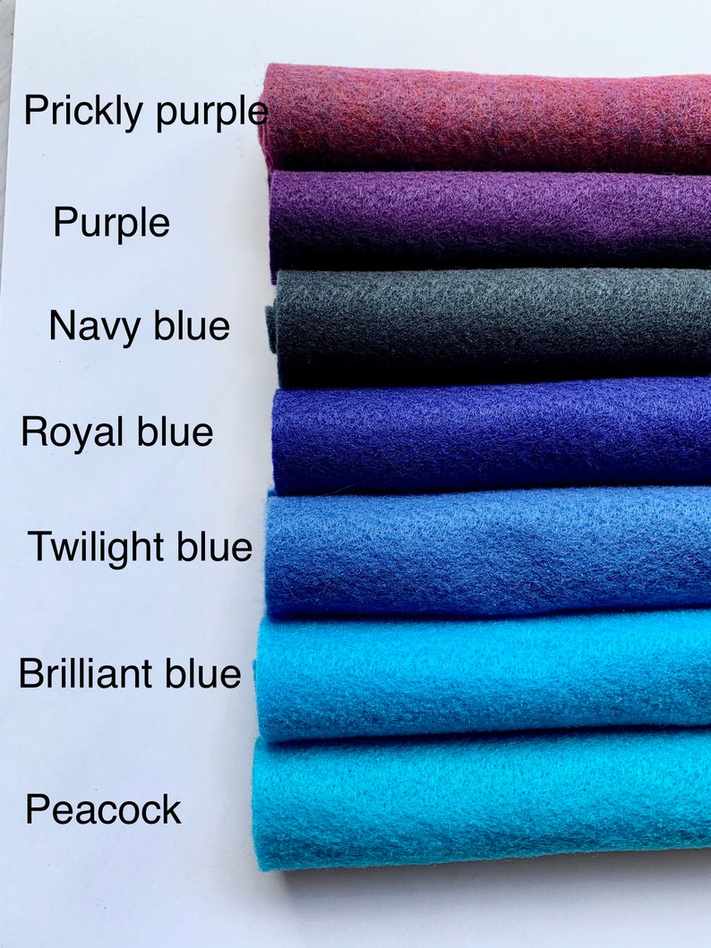 May include: A stack of seven felt fabric swatches in various shades of blue and purple. The swatches are labeled from top to bottom: Prickly purple, Purple, Navy blue, Royal blue, Twilight blue, Brilliant blue, and Peacock.