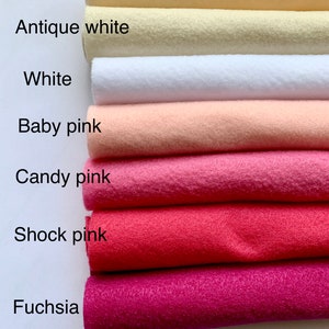May include: A stack of seven felt fabric swatches in various shades of pink, white, and cream. The swatches are labeled from top to bottom: Cream, Antique White, White, Baby Pink, Candy Pink, Shock Pink, and Fuchsia.