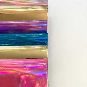 Op de afbeelding: Vijf vellen iriserende vinyl in verschillende kleuren, waaronder roze, goud, paars, blauw en zilver. De vellen zijn op elkaar gestapeld.
