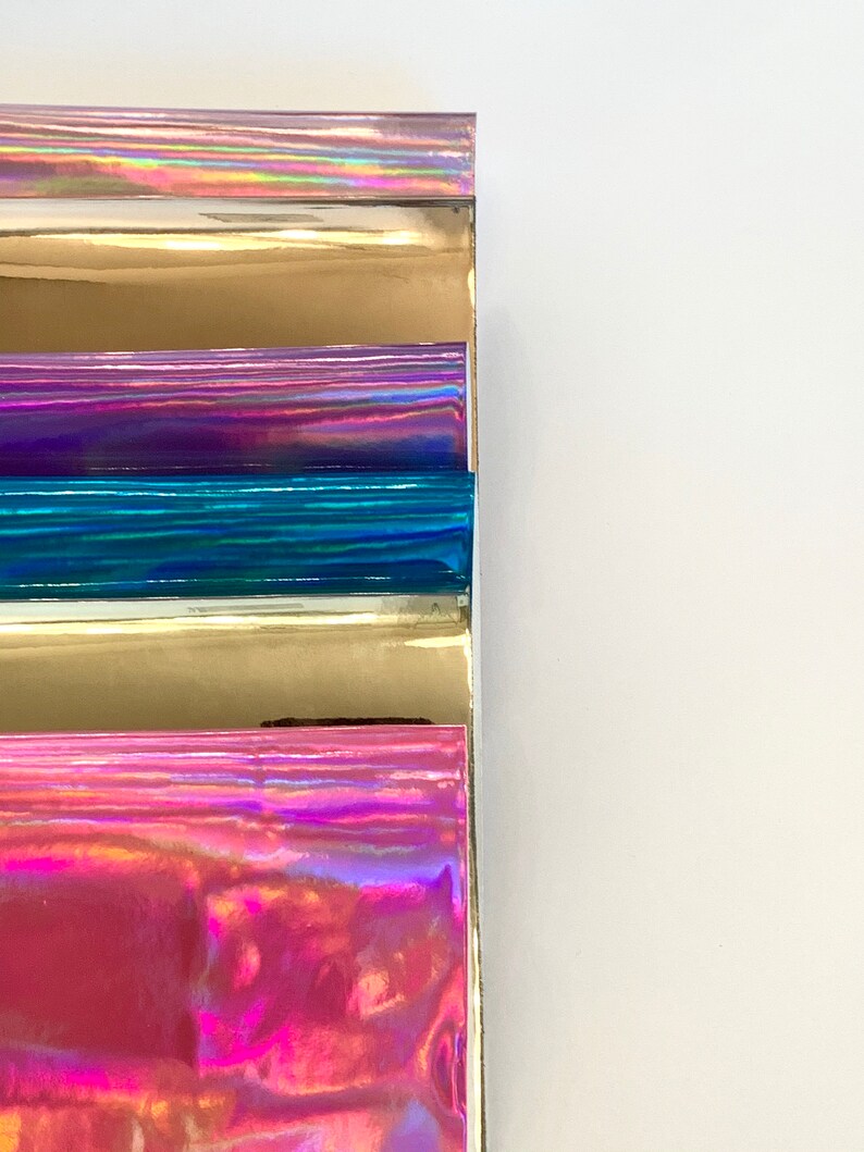 Op de afbeelding: Vijf vellen iriserende vinyl in verschillende kleuren, waaronder roze, goud, paars, blauw en zilver. De vellen zijn op elkaar gestapeld.