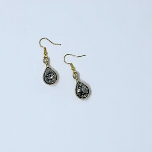 May include: A pair of silver teardrop earrings with a sparkly, textured finish. The earrings are on a white background.