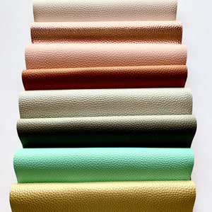 May include: A stack of eight different colored faux leather sheets. The colors are white, rose gold, pink, copper, cream, sage green, mint green, and gold.