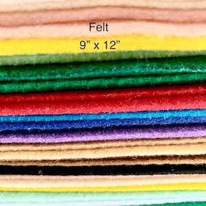 May include: A stack of felt sheets in various colors, including white, beige, pink, yellow, green, red, blue, purple, brown, black, and light blue. The felt sheets are 9 inches by 12 inches. The text "Felt 9" x 12" is printed on the top sheet.