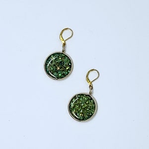 May include: A pair of green and gold earrings with a round, sparkly design.