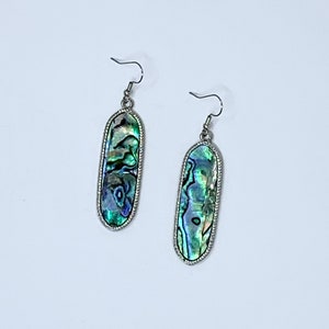 May include: A pair of silver dangle earrings with oval-shaped abalone shell inlays. The shell has a green, blue, and iridescent color pattern.