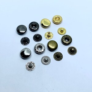 May include: Assortment of metal snap fasteners in various finishes, including gold, silver, and black. The snaps have a decorative design and are ideal for clothing, crafts, and other projects.