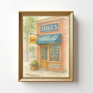 以下が含まれることがあります： 青い日よけと「LUKE'S」の文字が入ったレンガ造りの建物の水彩画。 「Luke's」と書かれた看板が日よけからぶら下がっています。 絵は金のフレームに入っています。 「STARS HOLLOW」の文字が窓の下にあります。