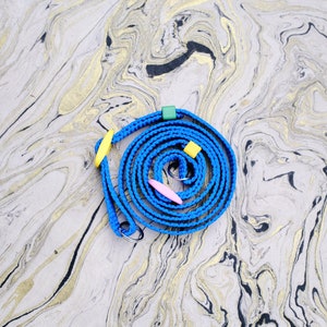 May include: A blue, coiled, adjustable strap with yellow, green, and pink accents. The strap has two metal rings and is on a white and gold marbled surface.