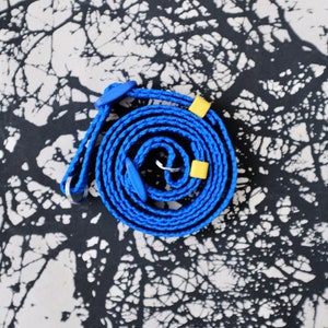 Puede incluir: Cuerda azul enrollada con detalles azules y amarillos. La cuerda está hecha de un material tejido y tiene un lazo en un extremo. El fondo es un patrón abstracto en blanco y negro.