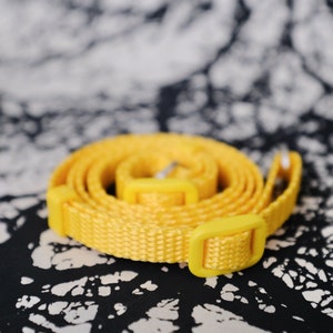 May include: A yellow woven strap with a plastic buckle. The strap is coiled and ready to be used.