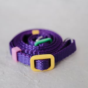 May include: A purple woven strap with yellow and green plastic buckles.