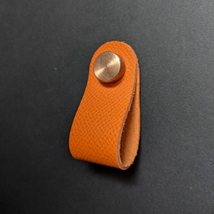 May include: Orange leather drawer pull with a round brass knob.