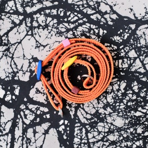 May include: An orange coiled leash with blue, yellow, and pink accents. The leash is on a black and white patterned background.