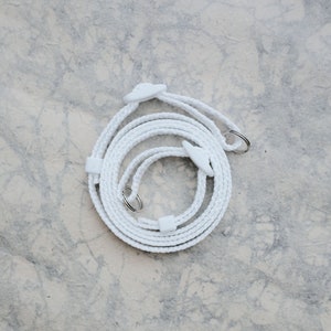 May include: White braided camera strap with two white plastic adjustable buckles and two silver metal rings.