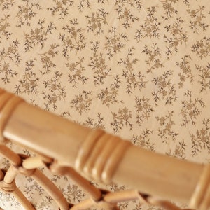 Può includere: Un cesto di vimini con una fodera in tessuto crema con un delicato motivo floreale. Il tessuto ha una lucentezza sottile e il cesto è fatto di rattan naturale intrecciato.