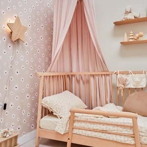 K&ouml;nnte beinhalten: Ein rosa Himmelbett mit einem Holzrahmen und Bettw&auml;sche mit Blumenmuster. Das Bett steht in einem Zimmer mit Blumenmuster-Tapete und einer sternf&ouml;rmigen Nachtischlampe aus Holz.