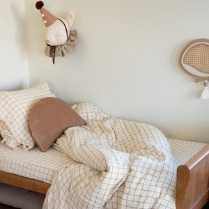 May include: A wooden bed with a brown and white checked bedding set. The bed has a brown headboard and a brown footboard. There is a brown pillow on the bed and a brown and white stuffed animal on the wall. There is a wooden whale wall decor with a woven pattern on the wall.
