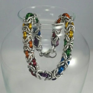 May include: A rainbow colored chainmail bracelet with a silver finish. The bracelet is made of small metal rings that are linked together in a pattern.