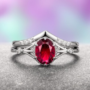 May include: A silver ring set with a large oval ruby gemstone surrounded by smaller diamonds. The ring has a delicate, intricate design with a V-shaped band.