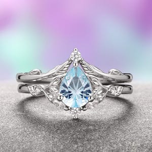 May include: A pear-shaped aquamarine gemstone ring set in a silver band with a delicate, leafy design. The ring is accented with smaller diamonds.