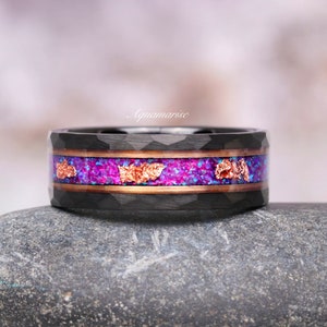May include: A black tungsten carbide ring with a hammered finish and a purple and copper inlay. The ring is sitting on a gray rock.