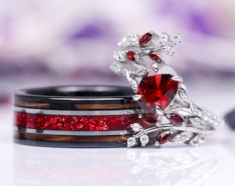 Könnte beinhalten: Ein Paar Eheringe. Der Verlobungsring hat einen großen roten Edelstein, der von kleineren roten Edelsteinen und weißen Diamanten umgeben ist, die in einer silbernen Fassung sitzen. Der Ehering ist aus schwarzem Holz mit roten und silbernen Akzenten.