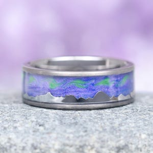 May include: A silver titanium ring with a purple and green aurora borealis design and a silver mountain range silhouette.