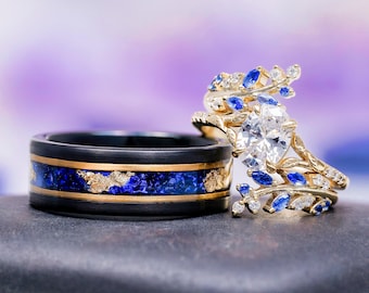 May include: A black band ring with a central inlay of blue crushed stone and gold flakes, paired with a gold ring featuring a large oval white center stone surrounded by marquise-cut blue stones and small clear stones in a leaf-like design.