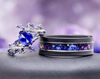 Puede incluir: Un anillo de plata con una gran piedra central azul ovalada rodeada de piedras azules más pequeñas de corte marquesa en una banda tipo enredadera, junto a un anillo de banda ancha negra con una incrustación central de material iridiscente azul y morado.