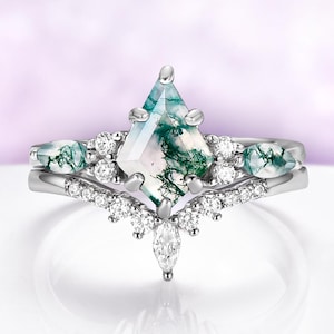 May include: A two-piece ring set featuring a silver band with a central kite-shaped moss agate stone. The main ring is accented with small, round, and marquise-cut clear stones. The moss agate has green and white patterns.