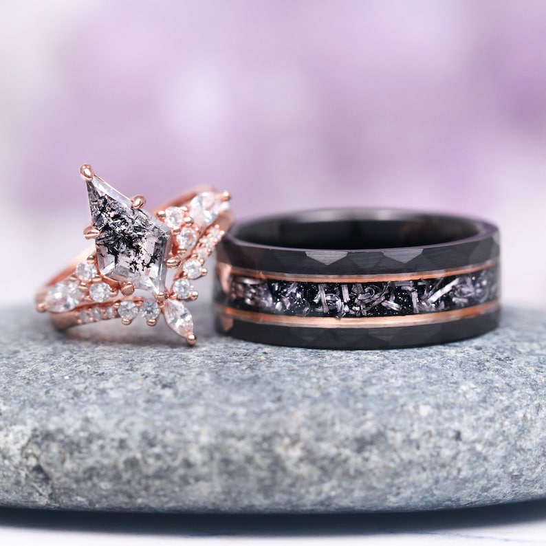 May include: A pair of wedding bands. The engagement ring features a rose gold setting with a large, clear, and black diamond. The wedding band is black with a rose gold inlay.