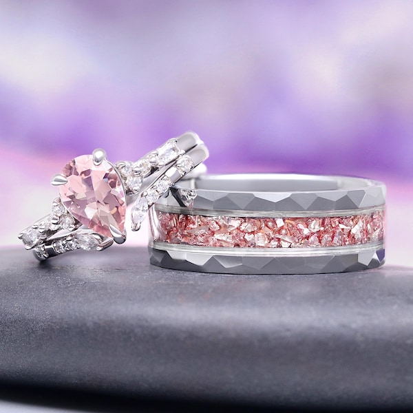 Op de afbeelding: Twee trouwringen. Eén ring heeft een peervormige roze edelsteen met omliggende accentstenen. De andere is grijs met een roze inleg van gemalen steen. De ringen staan tegen een vage paarse achtergrond.