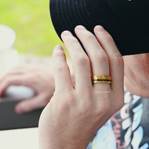 K&ouml;nnte beinhalten: Ein goldener Ring mit geh&auml;mmerter Oberfl&auml;che und einer Reihe gr&uuml;ner Edelsteine.